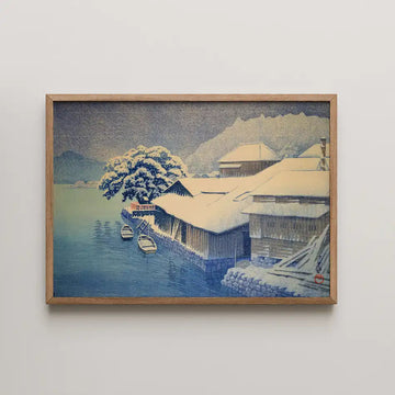 Hasui Kawase woodblock print titled Evening Snow at Ishinomaki, a snow covered pine beside timber warehouses with moored rowboats at a harbour.