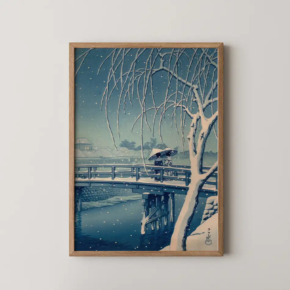 Hasui Kawase woodblock print of Evening Snow, Edo River, a snow covered willow over a wooden bridge as two figures cross beneath one umbrella.
