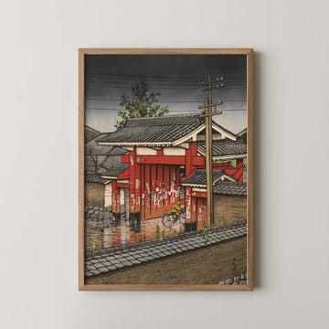 Hasui Kawase woodblock print of the Great Gate at Shiba, a red gate covered in paper charms as a cyclist rides past in the rain.