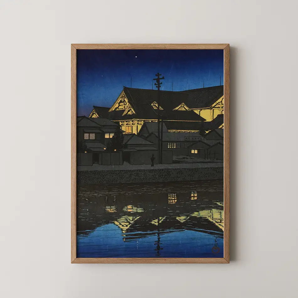 Hasui Kawase woodblock print of the Kabukiza theatre at night, its gabled roofs lit gold and reflected in the still river below.