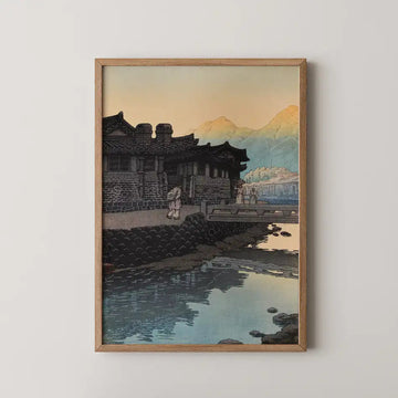 Hasui Kawase woodblock print of Kaesong in Korea at dusk, a stone walled house and figures crossing a footbridge over a stream.