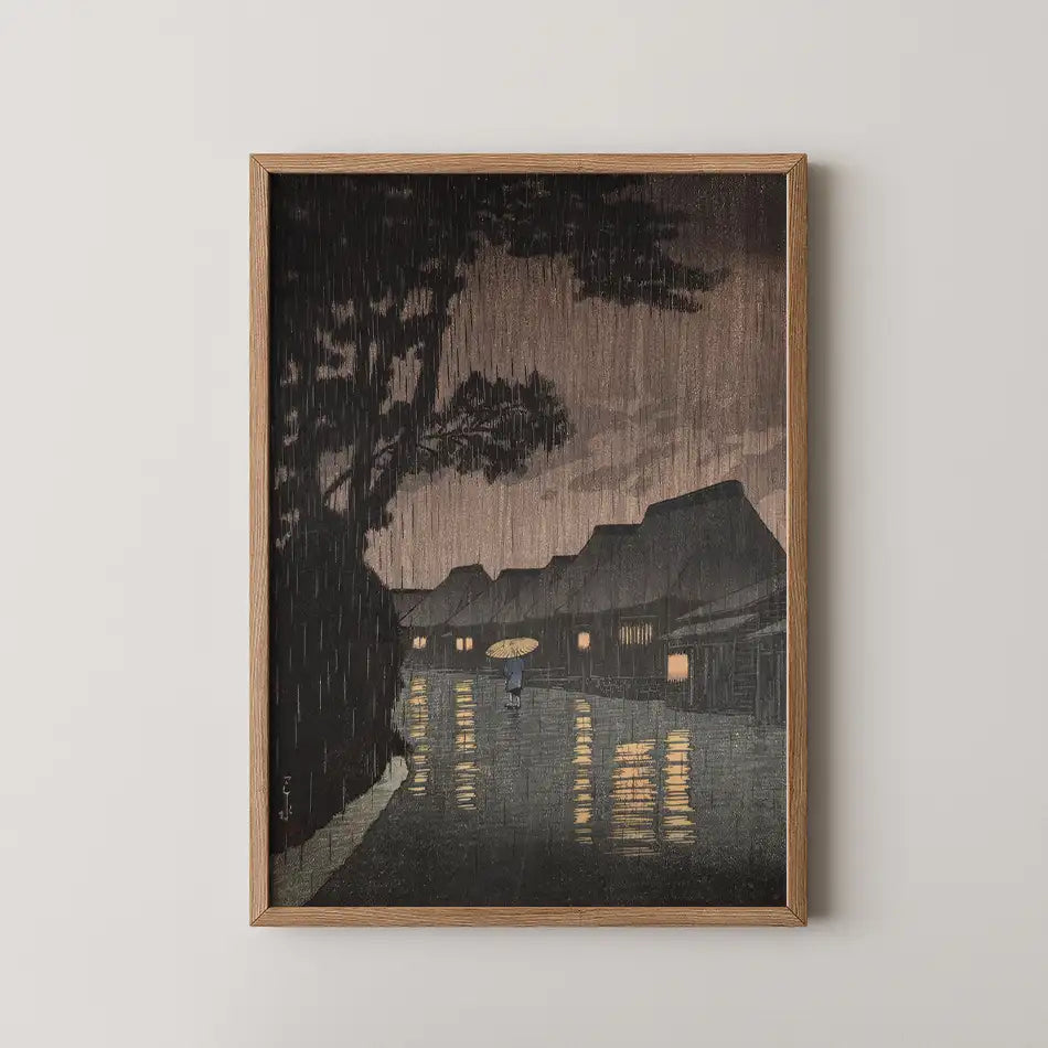 Hasui Kawase woodblock print of Rain at Maekawa, a figure with an umbrella walking a canal side street as heavy rain falls at night.