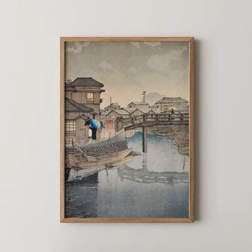 Hasui Kawase woodblock print of Shinagawa in the rain, a woman with a blue umbrella beside a moored boat on a canal lined with houses.
