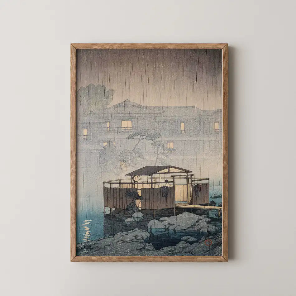 Hasui Kawase woodblock print of Shuzenji in Rain, a lantern lit bathhouse over a rocky river with a large hotel glowing through heavy rain.