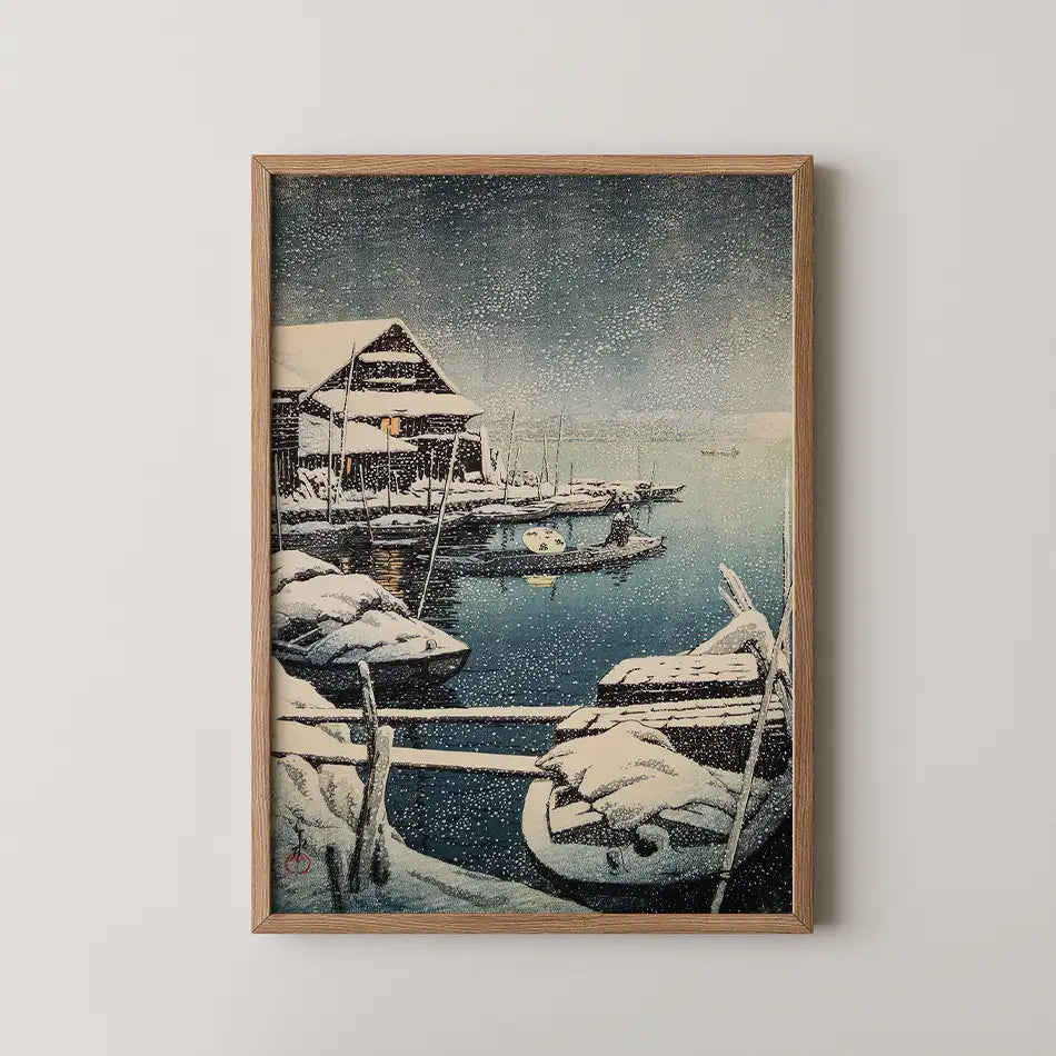 Hasui Kawase woodblock print of Snow at Mukojima, snow covered boats moored at a dock beside a lit lakeside house as snow falls.
