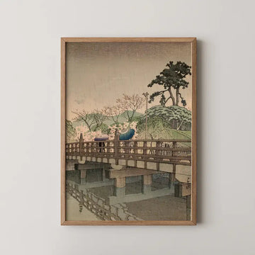 Hasui Kawase woodblock print of Spring Rain at Benkei Bridge, showing two figures crossing a wooden bridge under umbrellas as fine rain falls over blossoming trees.