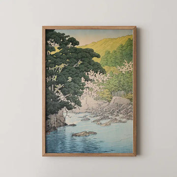 Hasui Kawase woodblock print titled Yugashima in Izu, showing a shallow turquoise river with grey boulders, dark pines leaning in from the left and cherry blossom on the far bank below a sunlit green hillside.