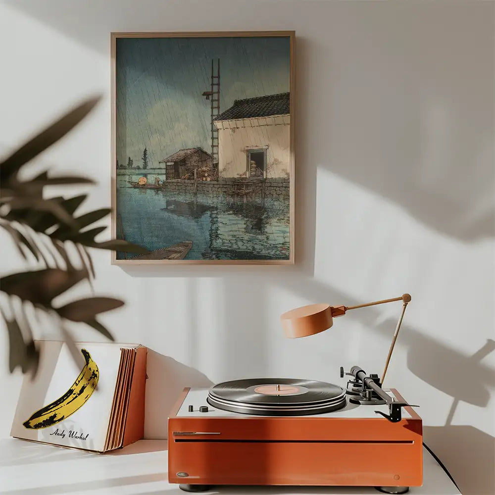 Painting of a tranquil waterfront scene with a traditional building, displayed above a vintage record player in a cozy interior setting.