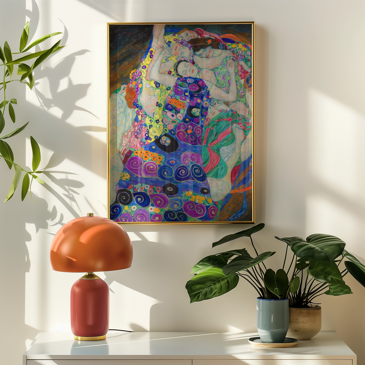 Colorful painting of figures embracing, framed and displayed on a wall above a stylish lamp and indoor plants.
