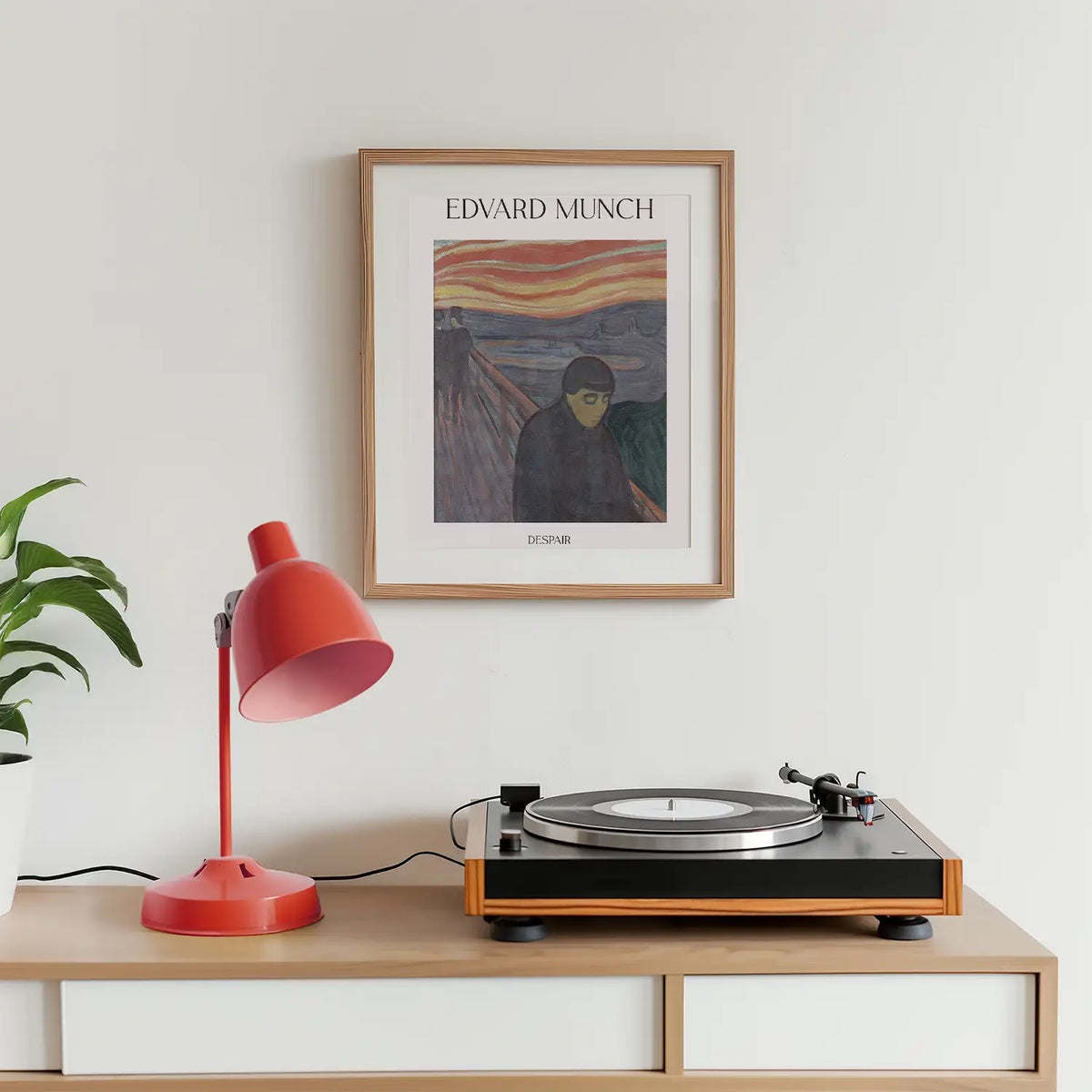 Framed poster of Edvard Munch's artwork "Despair," displayed on a wall above a turntable and a red desk lamp, with a green potted plant nearby.