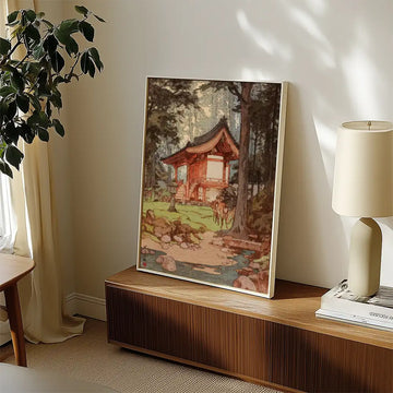Painting of a serene Japanese-style house surrounded by trees and rocks, displayed on a wooden surface in a well-lit interior setting.