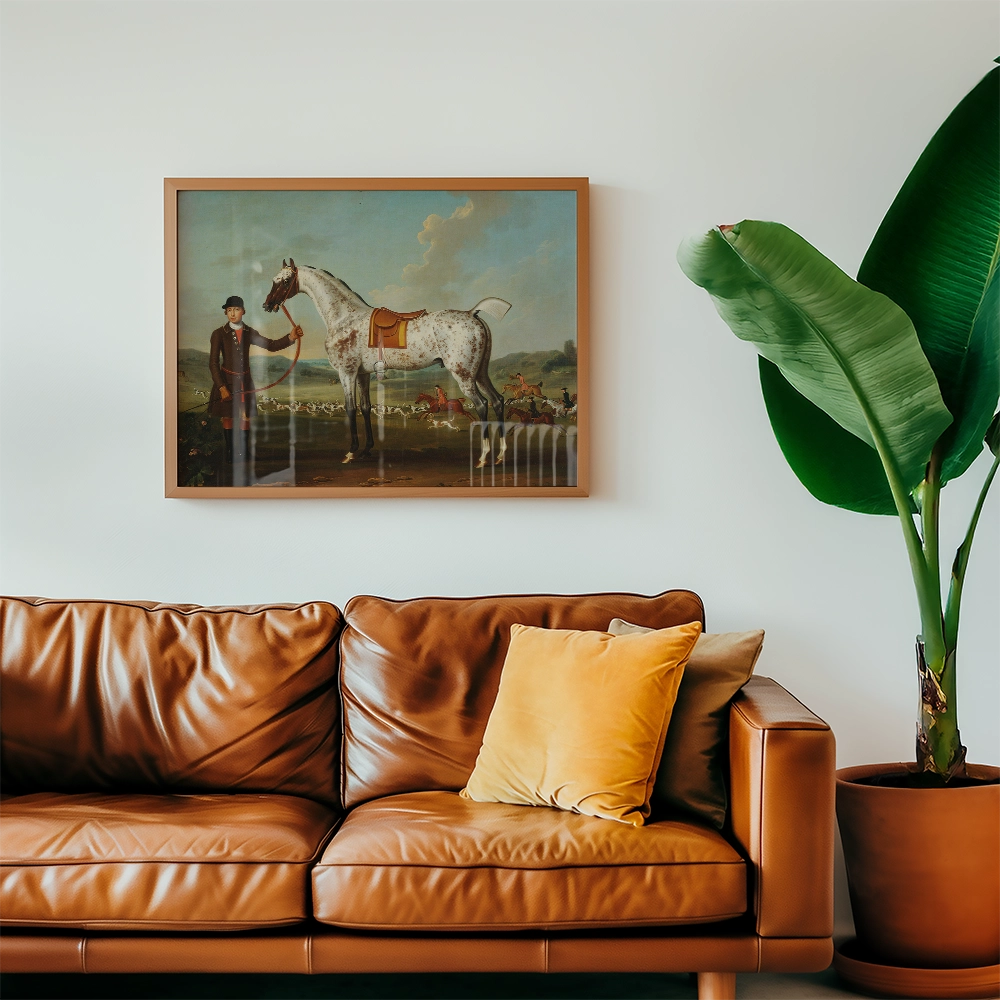 Painting of a horse and a rider in a landscape, framed and displayed above a brown leather couch with decorative pillows and a green plant.