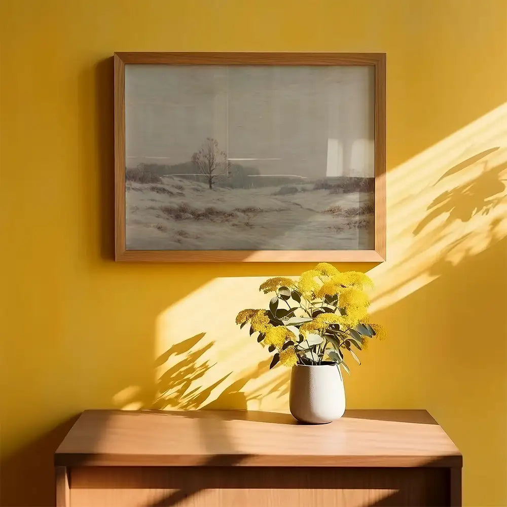 Framed painting of a winter landscape on a yellow wall, with a vase of yellow flowers on a wooden table in the foreground.