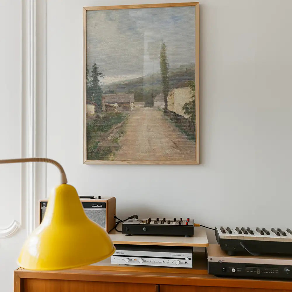 Framed landscape painting of a serene road with trees, displayed on a wall above a wooden console with vintage audio equipment and a yellow lamp.