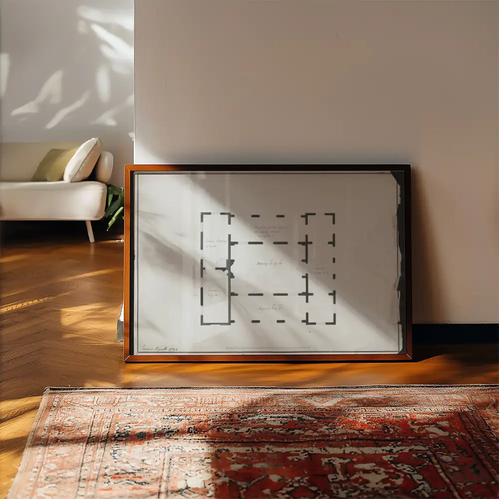 Framed abstract poster with a floor plan design, placed on a wooden floor beside a patterned rug and a cozy living room setting.
