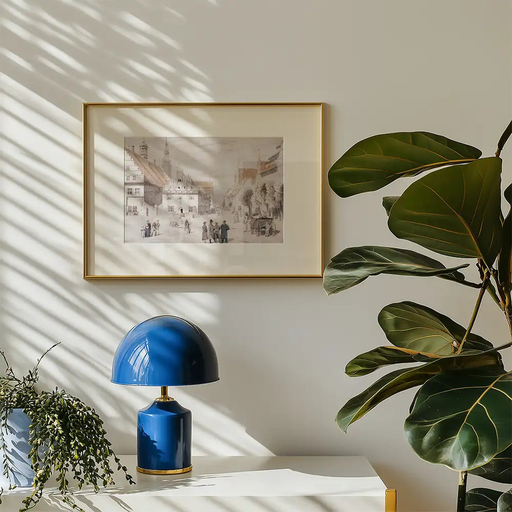 Framed artwork featuring a historical street scene, displayed on a light wall with a blue lamp and a leafy plant nearby
