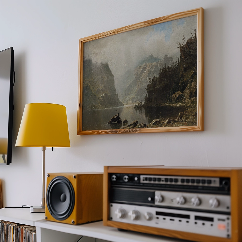 Framed landscape painting of mountains and a river, displayed on a wall above a yellow lamp and vintage audio equipment.