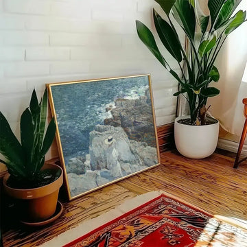 Painting of a coastal scene featuring rocks and water, displayed in a stylish interior setting with plants and warm wood accents.