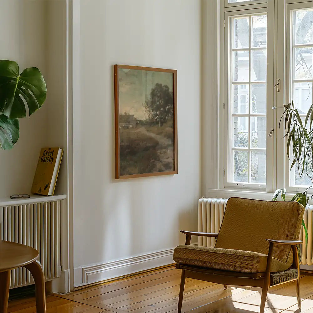 Framed landscape painting on a wall in a cozy living room with a brown armchair and a green plant.