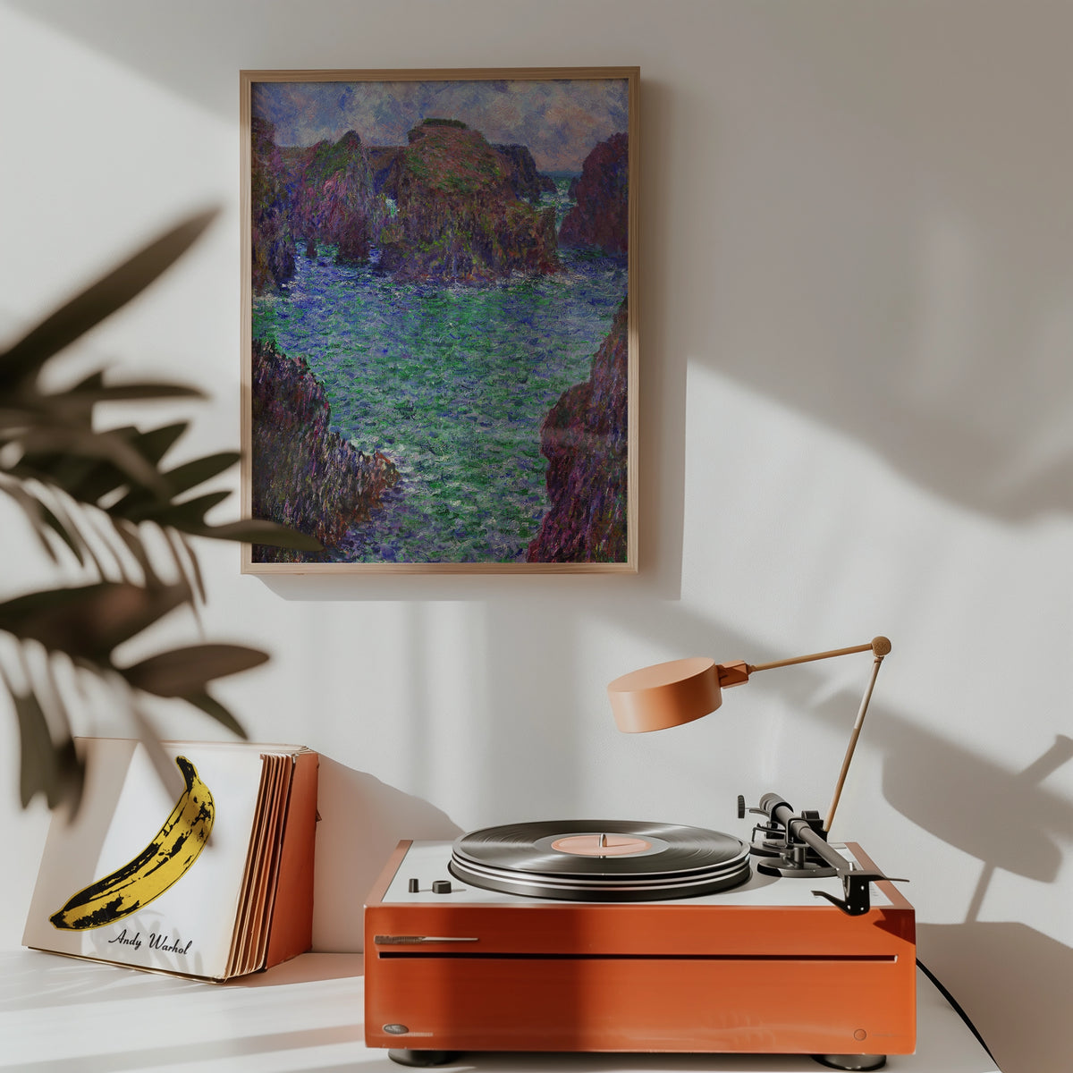 Framed painting of a serene coastal landscape featuring rocky outcrops and vibrant green water, displayed above a vintage record player in a stylish interior setting.