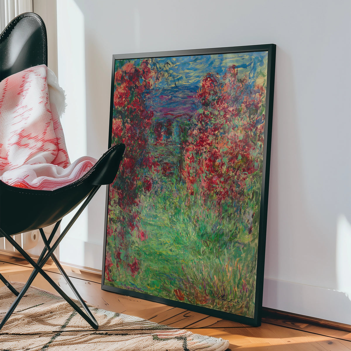 Colorful painting featuring vibrant red flowers and lush green foliage, displayed near a black chair in a well-lit interior setting.