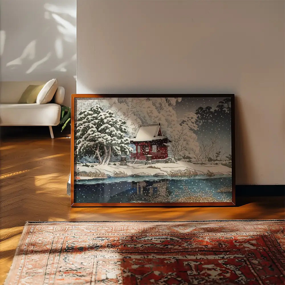 A framed painting of a red house surrounded by snow-covered trees, reflected in a calm body of water, set against a cozy interior backdrop.