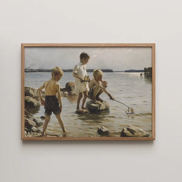 Painting of three children playing by the water, one boy launching a toy sailboat and two others observing, framed in wood.