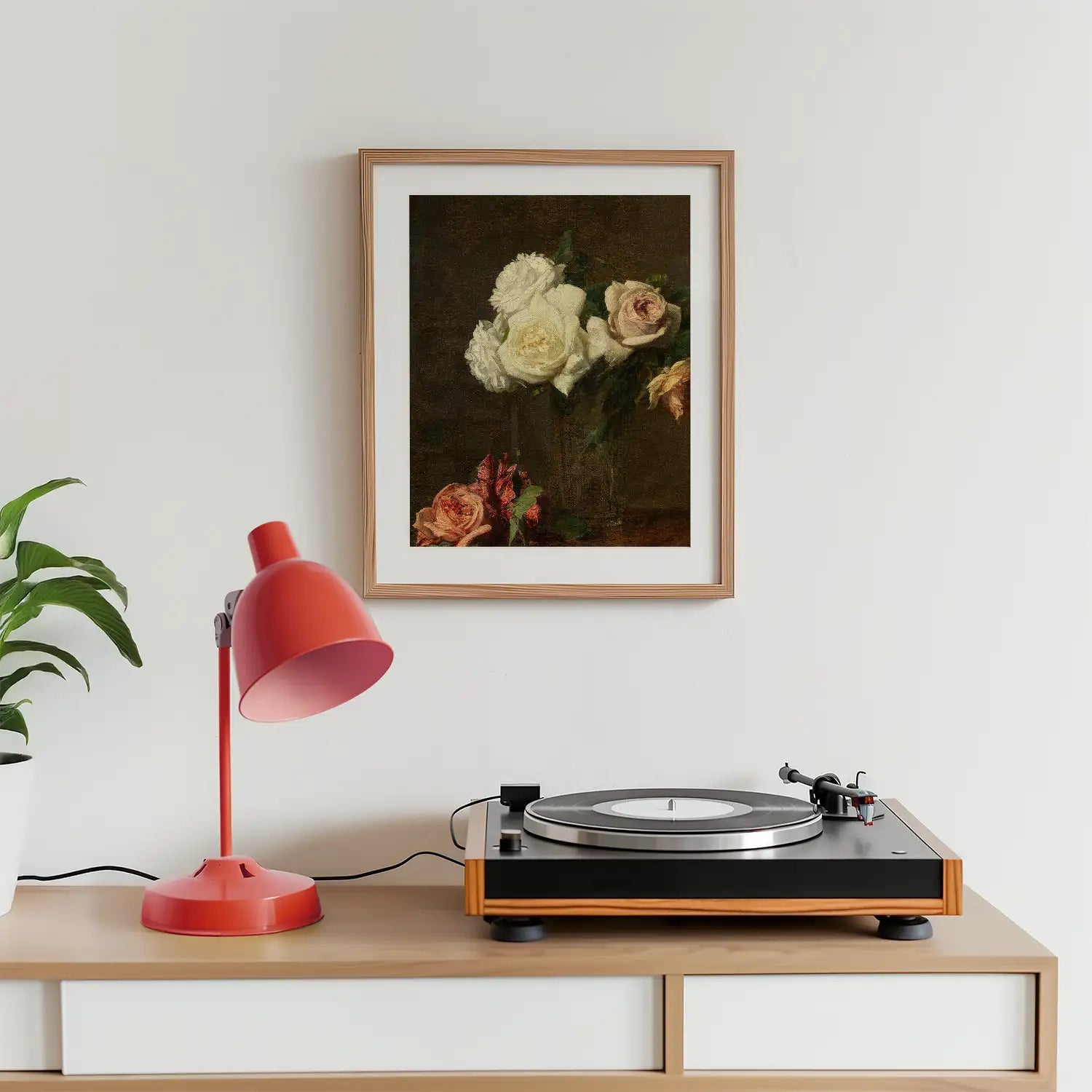 Framed painting of white and pink roses on a dark background, displayed on a wall above a wooden table with a red lamp and a record player.