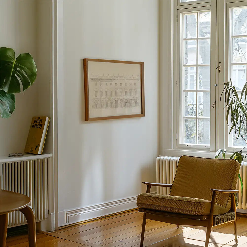 Framed monochromatic architectural sketch painting on a white wall in a cozy living room setting with a brown chair and potted plant.