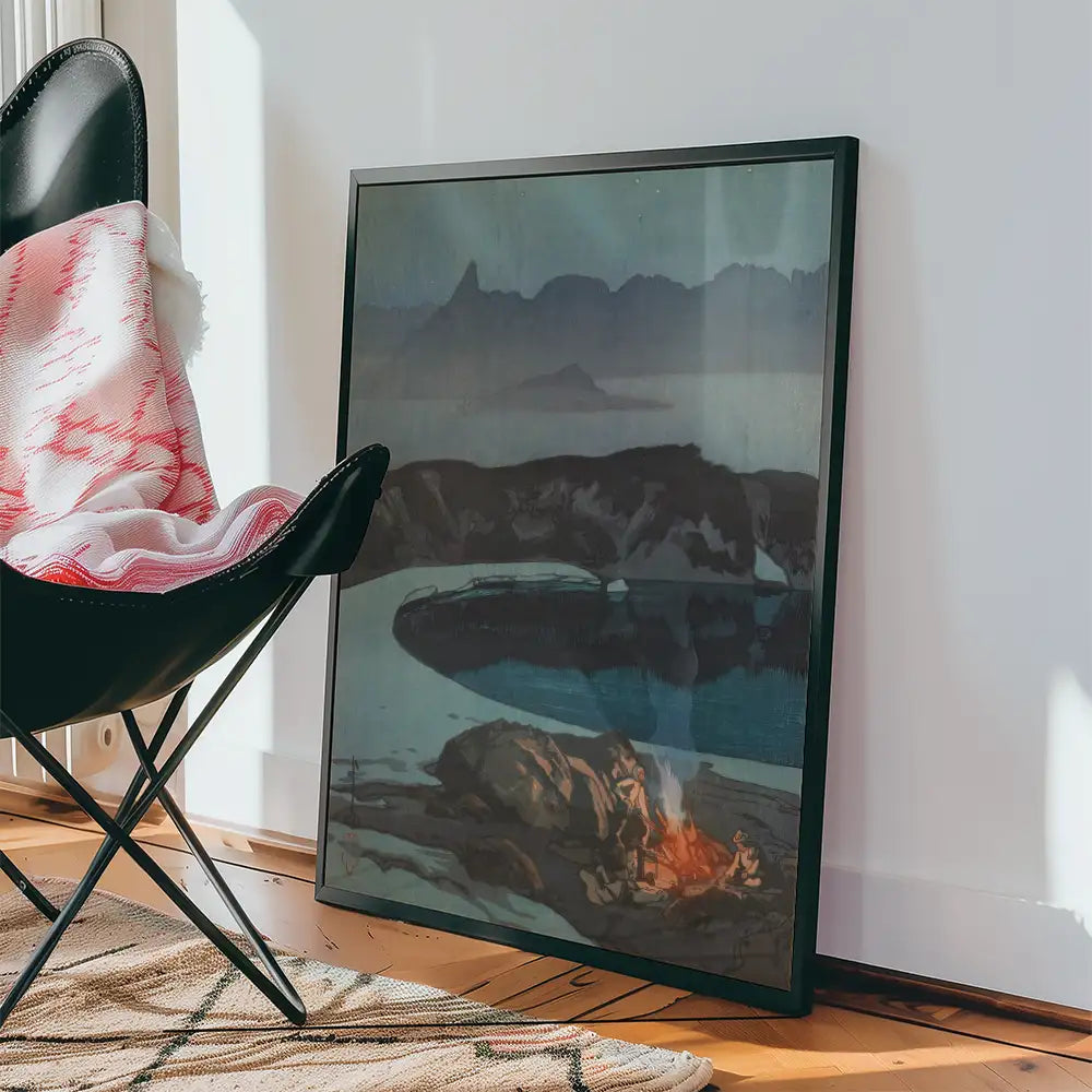Framed painting leaning against a wall, featuring a serene landscape with water and mountains, accompanied by a black chair and a cozy blanket.