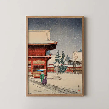 Framed painting of a traditional Japanese scene with two figures walking in the snow near a red temple and evergreen trees.