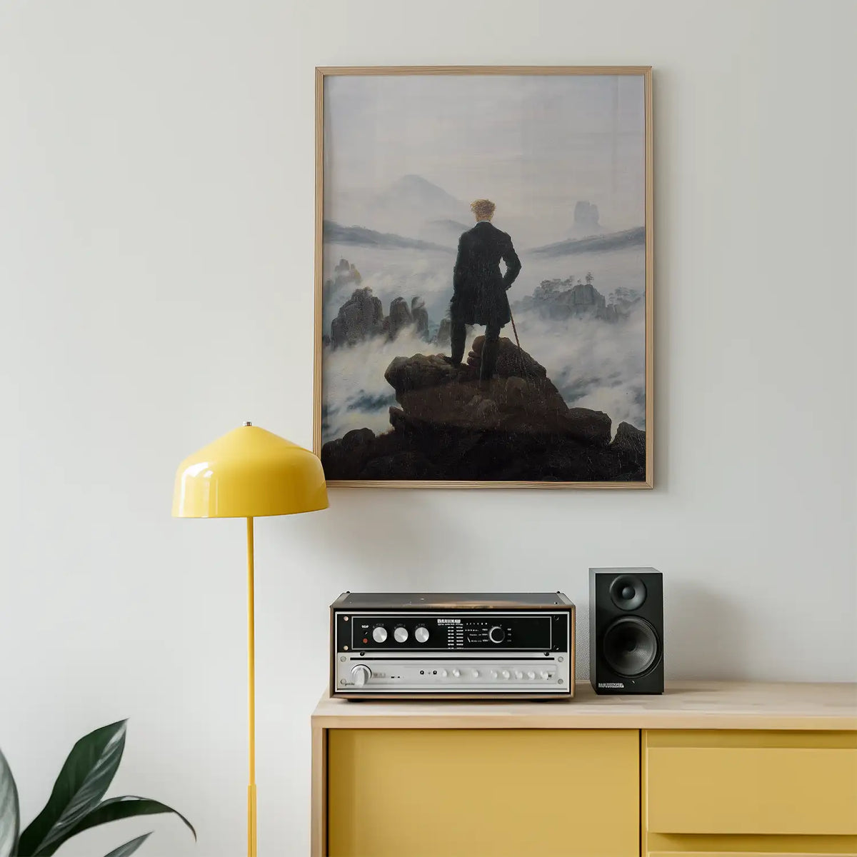 Framed painting of a man standing on a rocky outcrop overlooking a foggy landscape, displayed above a mid-century modern sideboard with a yellow lamp and a vintage audio system.