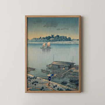 Framed painting of a serene riverside scene depicting boats on water, a small house, and a figure walking with an umbrella under a cloudy sky.