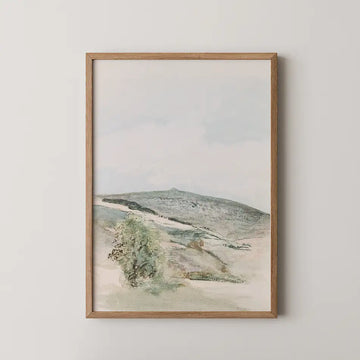 Framed painting of a serene landscape featuring rolling hills and a cloudy sky.