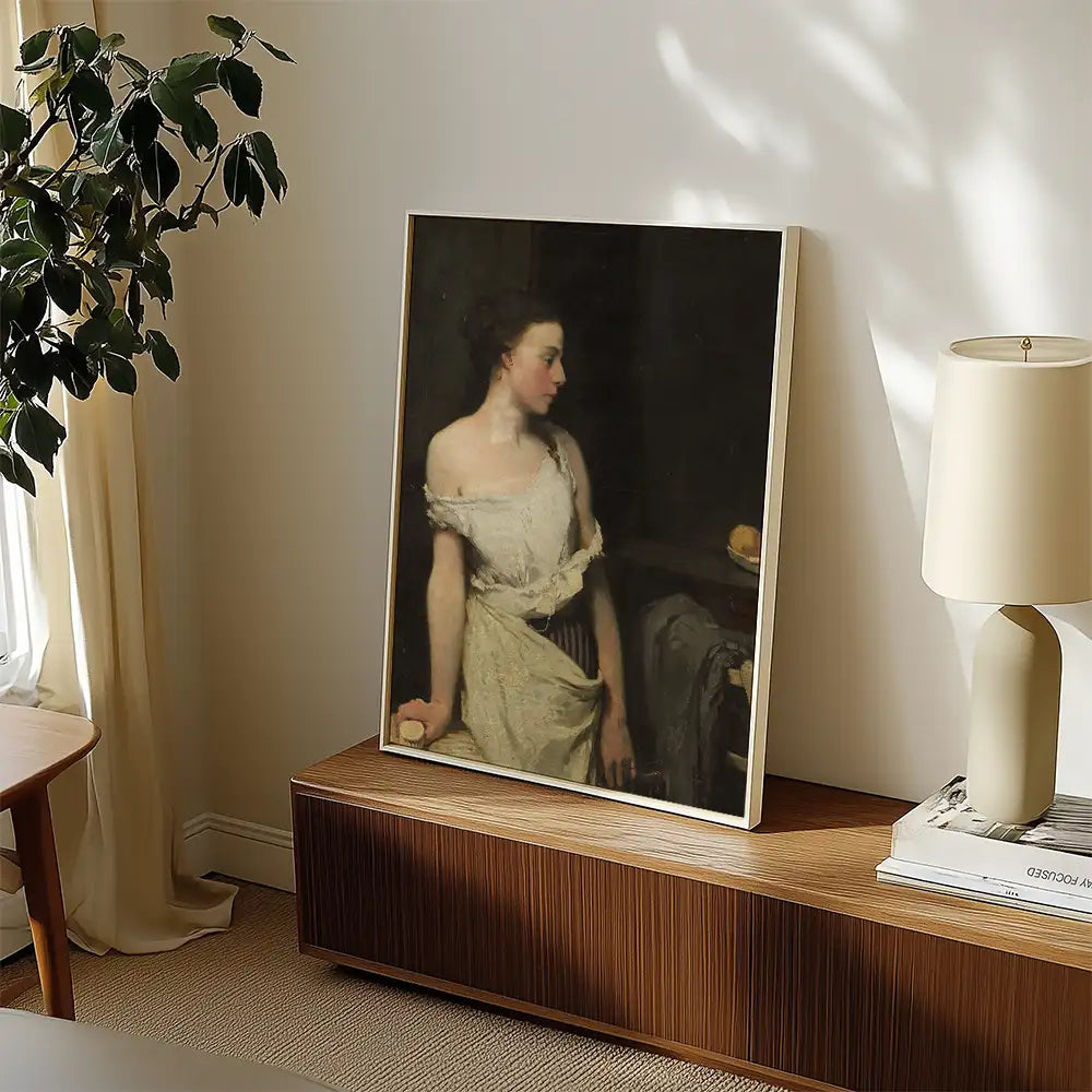 A framed painting of a woman in a historical dress, displayed in a modern interior setting with a plant and lamp nearby.