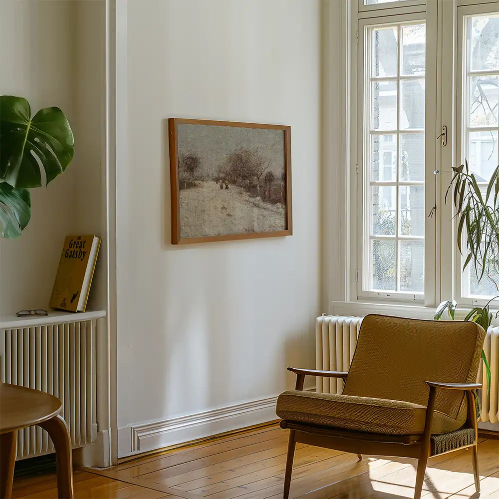 Framed painting of a landscape hanging on a white wall in a cozy living room with a brown armchair and a potted plant.
