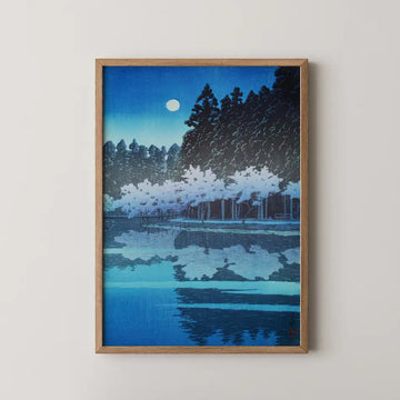 A framed painting of a tranquil night scene featuring trees and a moon reflecting on a calm body of water, predominantly in shades of blue.